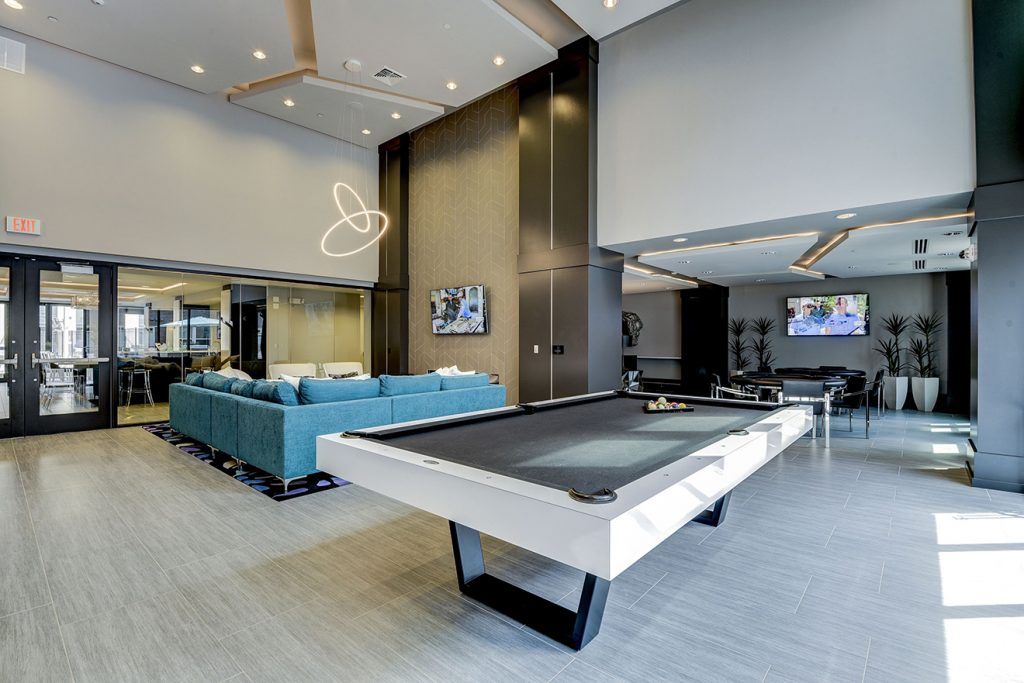 Community gaming area with large pool table, card tables, and sectional sofa near wall-mounted TV