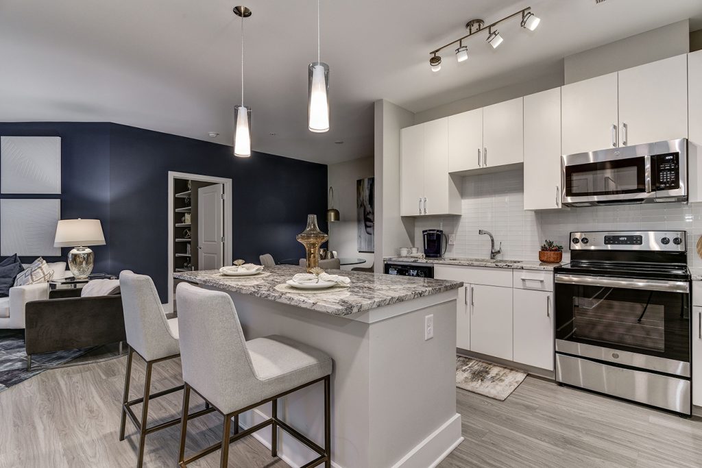 Model apartment with open-plan kitchen, white cabinets, large kitchen island, and pendant lighting