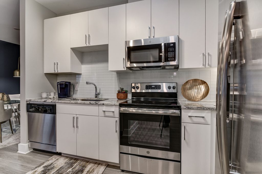Model apartment kitchen with white cabinets, subway tile backsplash, and stainless steel appliances