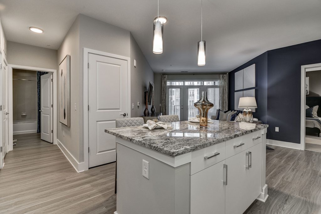 Model apartment with kitchen island, pendant lighting, and dark gray accent wall