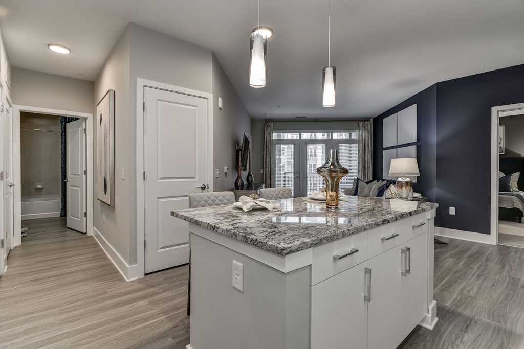 Model apartment with kitchen island, pendant lighting, and dark gray accent wall