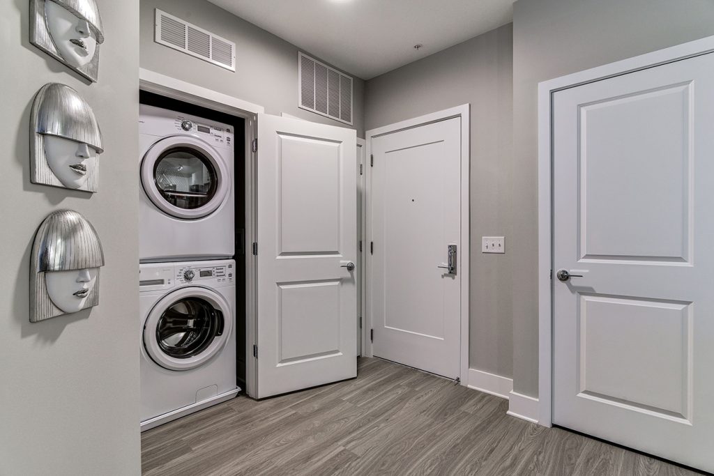 Model apartment entryway with coat closet and full size washer and dryer machines