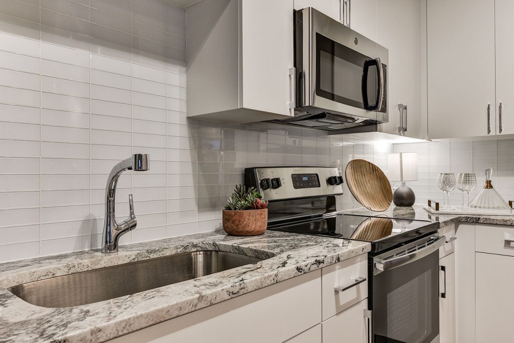 Model apartment kitchen with subway tile, granite countertops, and stainless steel appliances
