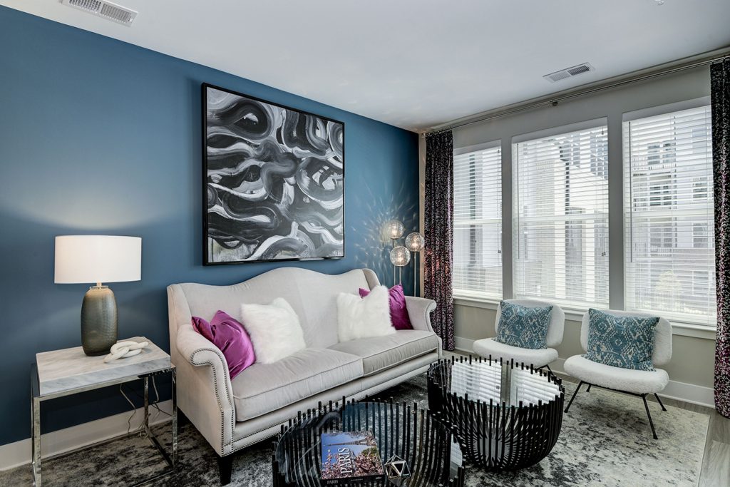 Model apartment living room with blue accent wall, loveseat, and accent chairs