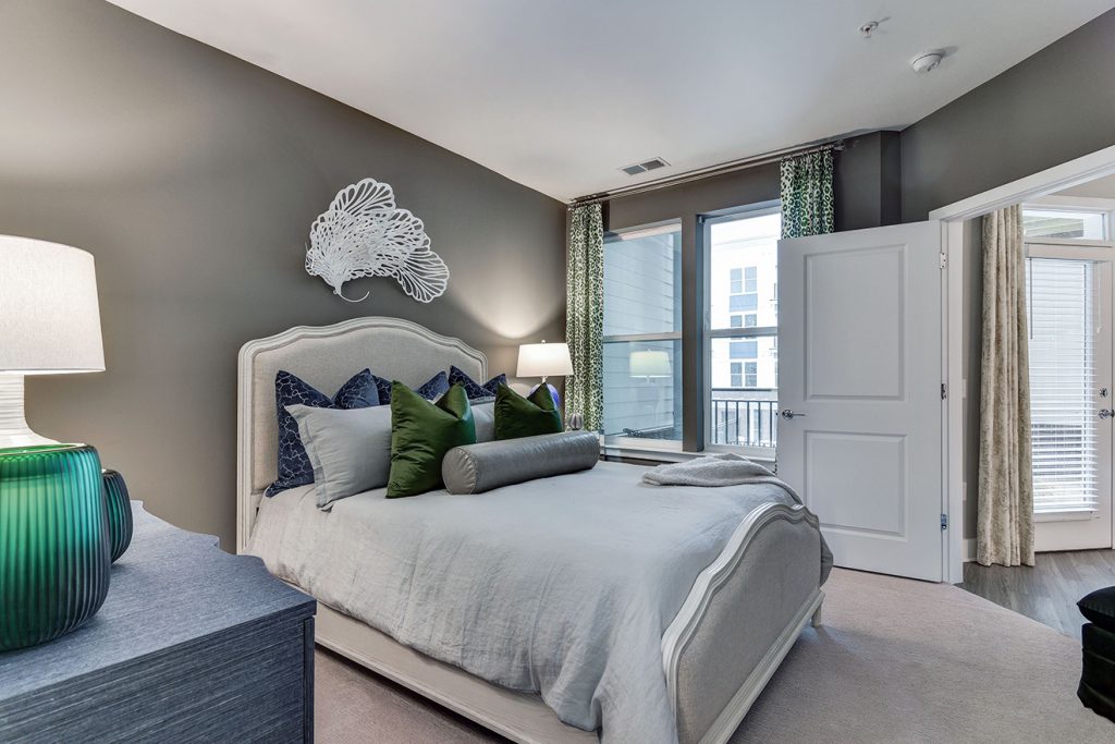 Model apartment kitchen with carpeted floors, Queen bed, and window to balcony