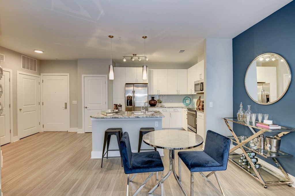 Model apartment kitchen and dining area with small table, kitchen island, and wood-style flooring