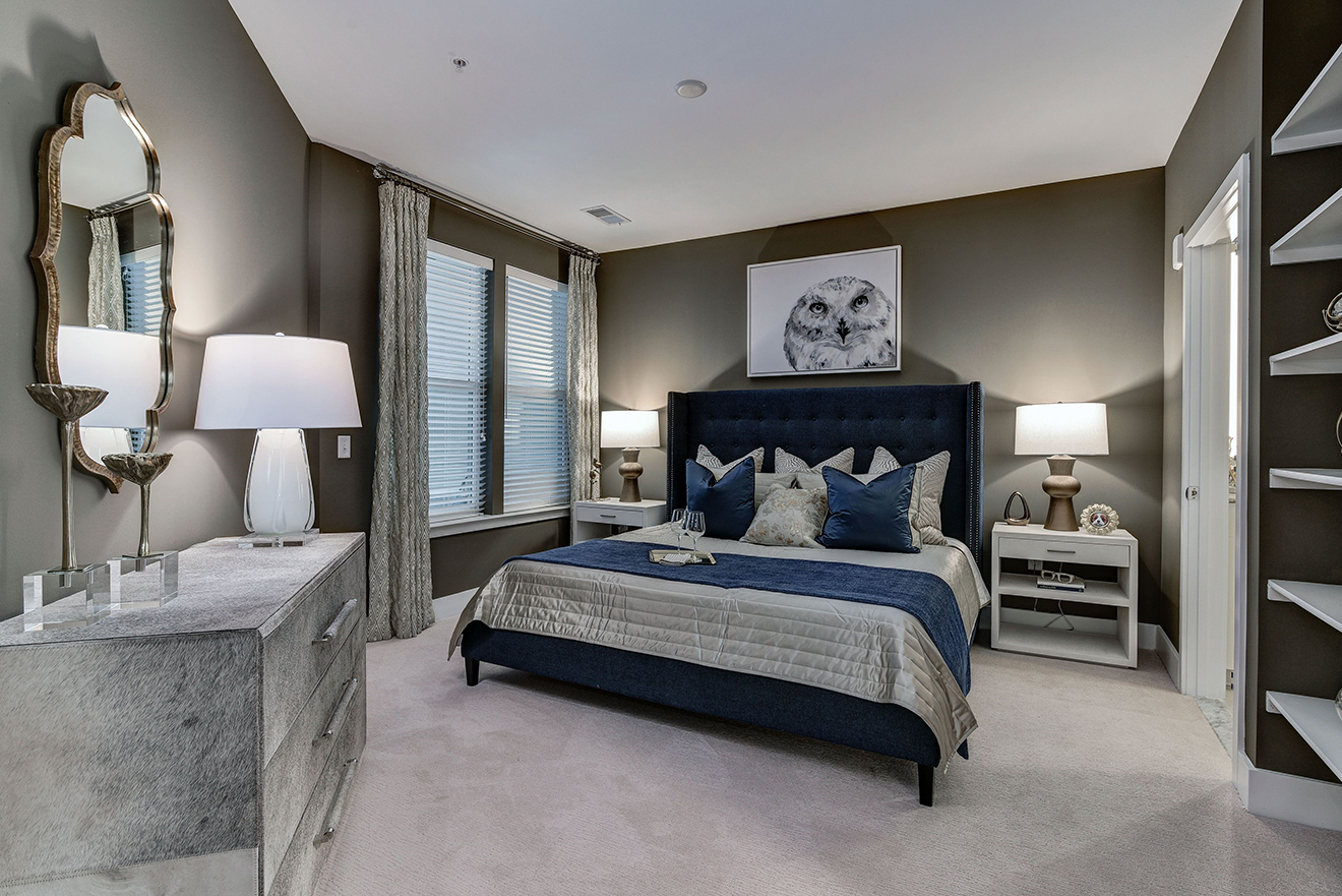 Model apartment bedroom with king-size bed, carpeted floors, and built-in bookcases