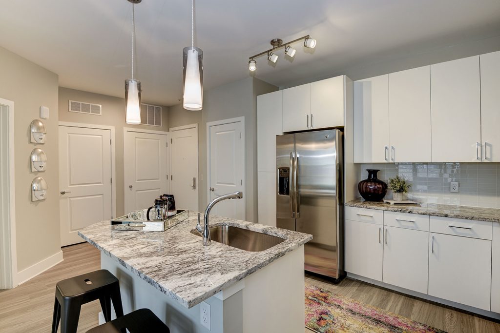 Model apartment kitchen with granite countertops, white cabinets, stainless steel appliances, and pendant lighting