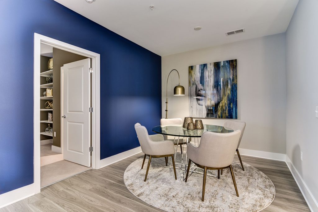 Model apartment dining area with five-piece dining set, blue accent wall, and wood-style flooring