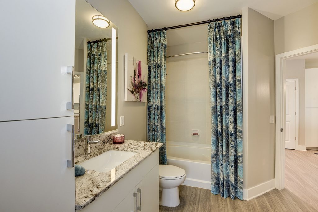 Model apartment bathroom with granite countertop, single-vanity sink, and curtained tub