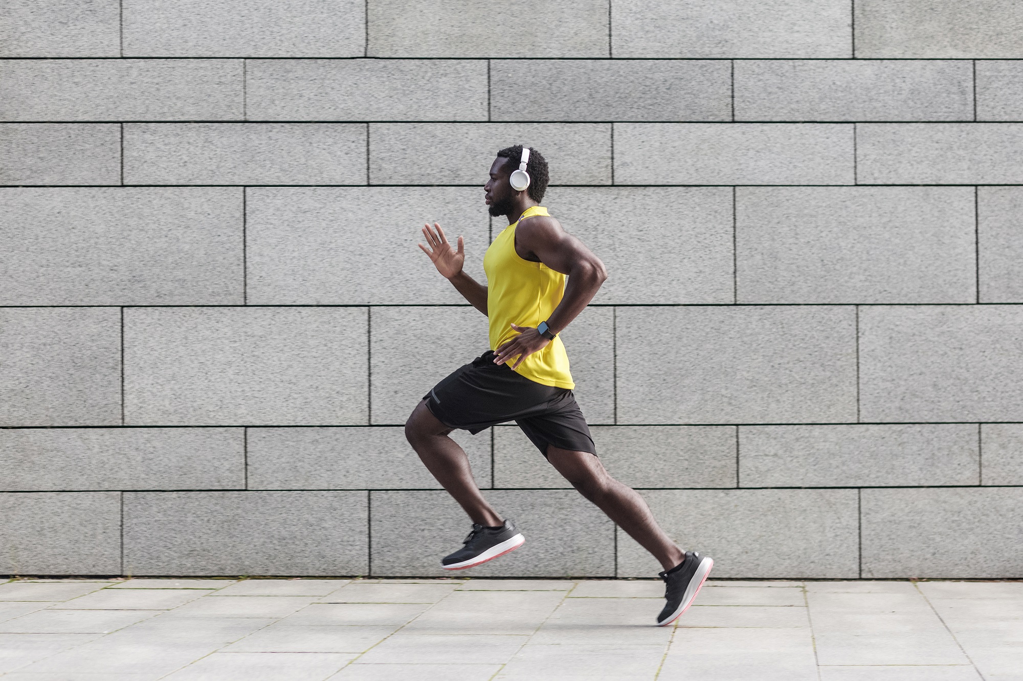 Man with headphones, yellow top and black shorts running down street
